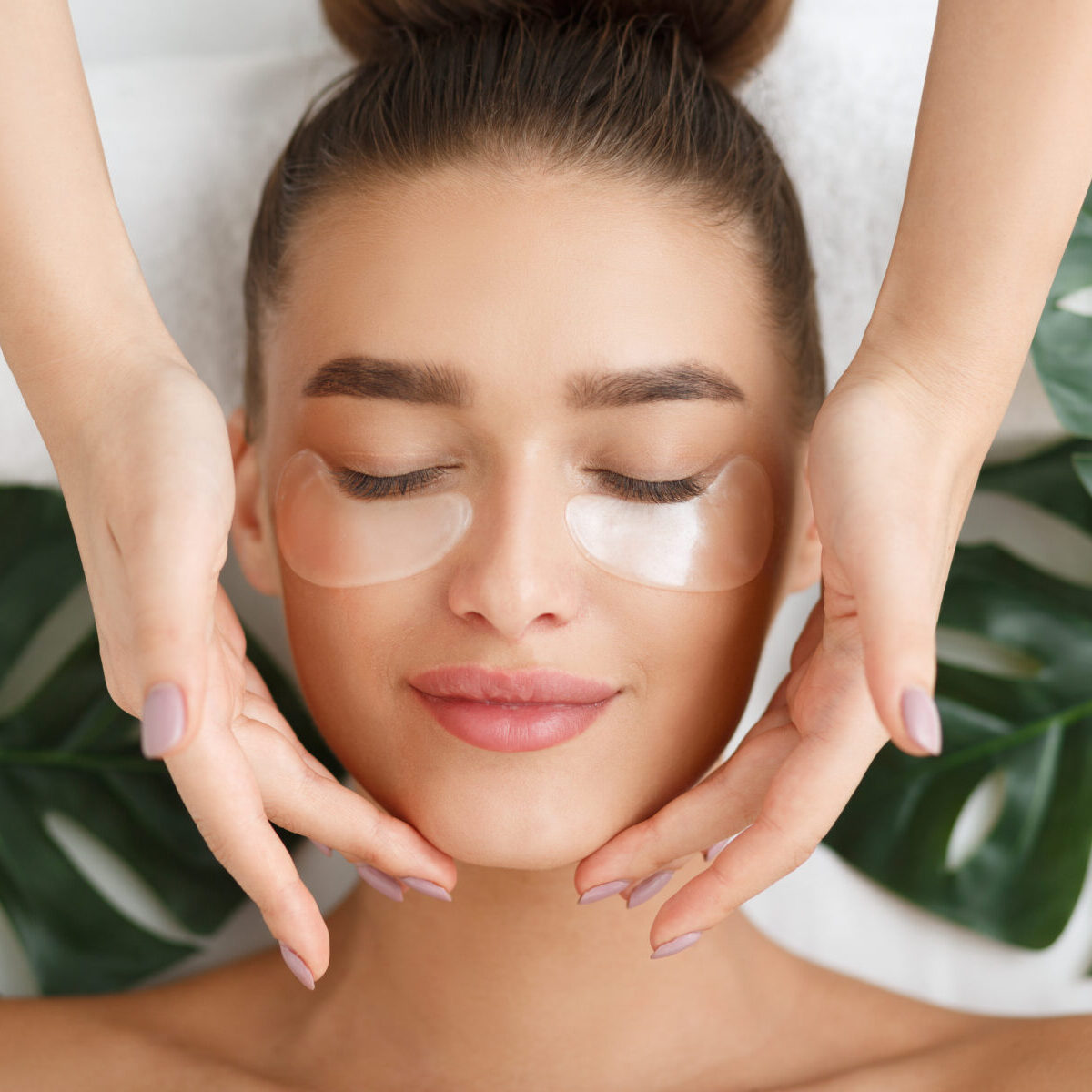 Woman with eye patches having face massage at beauty salon